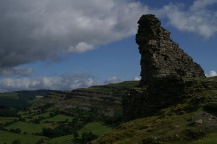A ruined hill fort with a rocky escarpment behind it