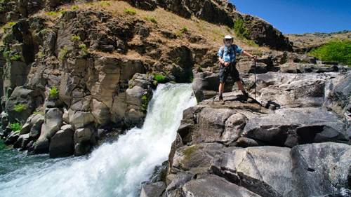 A person standing on rocks near a waterfall

Description automatically generated