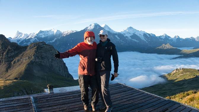 Two men standing on a roof with mountains in the background
Description automatically generated