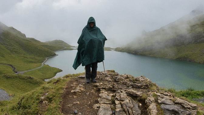 A person standing on a rock with a rain poncho
Description automatically generated