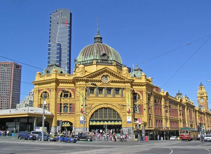 A large building with a dome roof with Flinders Street railway station in the background

Description automatically generated